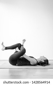 Young European Brunette Woman Doing Reclining Pigeon Pose, Also Called Supine Pigeon, Dead Pigeon, Eye Of The Needle, Or Threading The Needle Pose Or Supta Kapotasana. Black And White Vertical View.