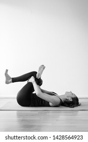 Young European Brunette Woman Doing Reclining Pigeon Pose, Also Called Supine Pigeon, Dead Pigeon, Eye Of The Needle, Or Threading The Needle Pose Or Supta Kapotasana. Black And White Vertical View.