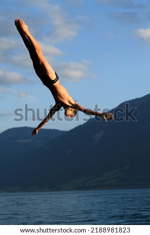 young european diver performs an element of jump on the shore of a lake in a mountainous area. 