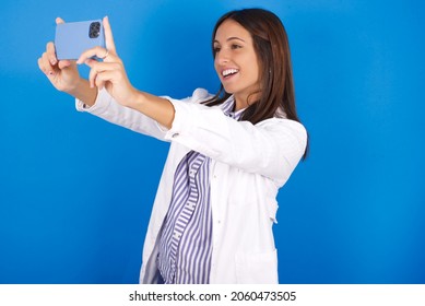 Young European Doctor Woman On Blue Background Taking A Selfie To Post It On Social Media Or Having A Video Call With Friends.