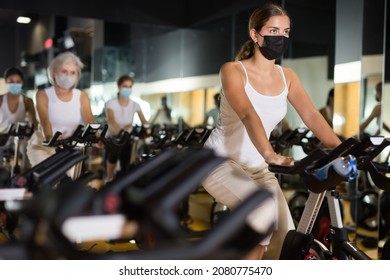 Young European Female In Protective Mask Riding Exercise Bike During Cycling Class In Gym