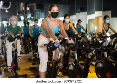 Young European Female In Protective Mask Riding Exercise Bike During Cycling Class In Gym