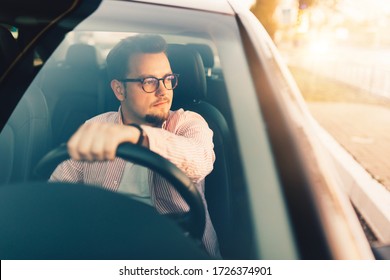 A young european happy driver in comfortable expensive car. Stylish man wearing glasses. View through the windshield