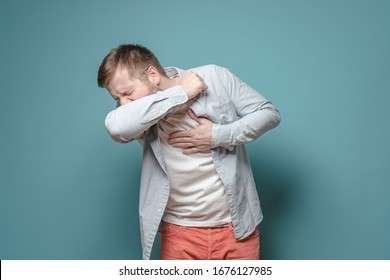 Young European man coughs at elbow and holds hand on chest, experiencing pain. Concept of the spread of the virus. - Shutterstock ID 1676127985