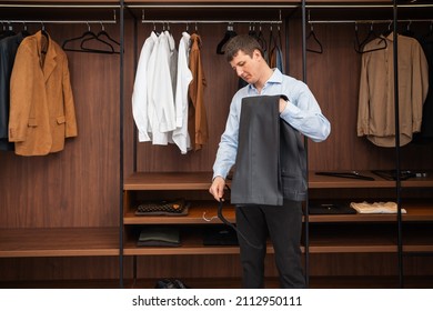 Young European Man With Dark Hair Brings Wardrobe Order Puts Everything In Its Place. Closet Organized. Man Chooses Clothes. Capsule Wardrobe For Men.