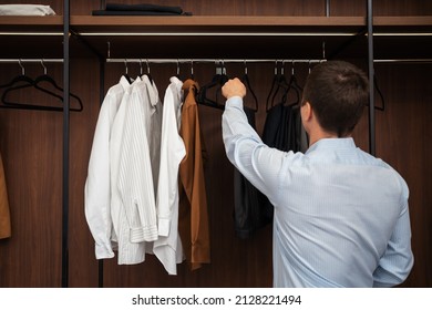 Young European Man With Dark Hair Brings Wardrobe Order Puts Everything In Its Place. Closet Organized. Man Chooses Clothes. Capsule Wardrobe For Men.