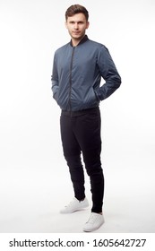 Young European Man In White Sweater And Black Pants, Blue Bomber Jacket Posing On White Background. Isolated.