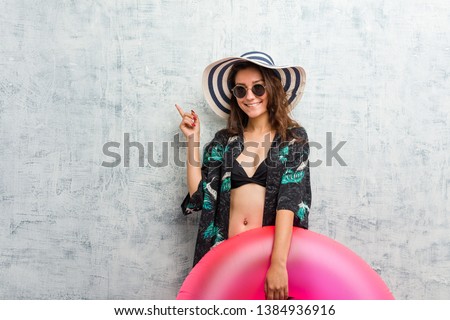 Young european woman holding a inflatable donut smiling cheerfully pointing with forefinger away.