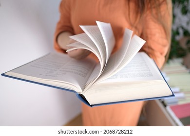 young european woman with long hair holds a thick book in a blue cover in her hands, flips through the pages, concept of fiction, nonfiction, reading, developing hobby - Powered by Shutterstock