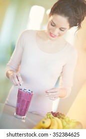 Young European Woman Making Fresh Berry Smoothie In Kitchen. Healthy Eating Concept. Full Glass Of Healthy Juice.