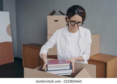 Young European Woman Packing Carton Container And Puts Textbooks Into. Happy Girl In Glasses Is Stacking Books Into Boxes. Female Student Moves To Rental Apartment. Relocation And Entering To College.