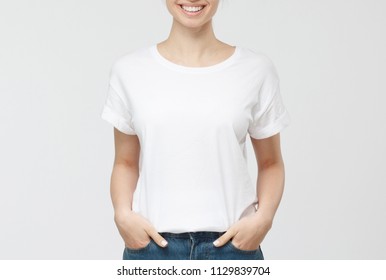 Young European Woman Standing With Hands In Pockets, Wearing Blank White Tshirt With Copy Space For Your Logo Or Text, Isolated On Grey Background