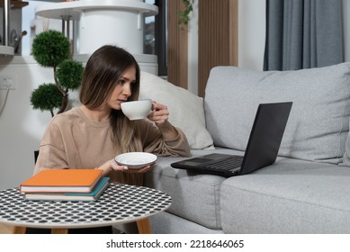 Young Exchange Student Drinking Tea Or Coffee In Her Apartment While Talking On Video Call On Laptop With Her Family In Different Country. Computer Programmer Taking A Break From Work At Home. 