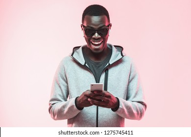 Young Excited African American Man Looking At His Phone With Surprise Expression And Mouth Wide Open, Isolated On Pink Background 