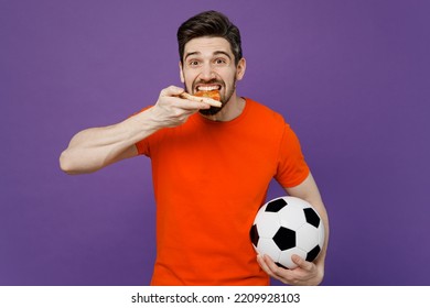 Young Excited Amazed Fan Man He Wears Orange T-shirt Cheer Up Support Football Sport Team Hold In Hand Soccer Ball Eat Slice Of Italian Pizza Watch Tv Live Stream Isolated On Plain Purple Background