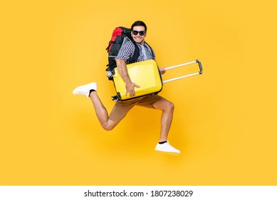 Young excited Caucasian male tourist with baggage jumping in mid-air ready to travel isolated on colorful studio yellow background - Shutterstock ID 1807238029