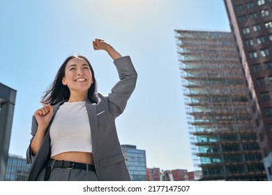 Young excited confident proud Asian business woman winner wearing suit standing on street, raising hands, feeling power, motivation, energy, celebrating career financial success in big city outdoors. - Shutterstock ID 2177147507