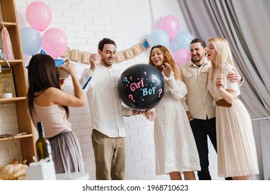 Young excited couple blowing up surprise balloon during gender reveal party indoors