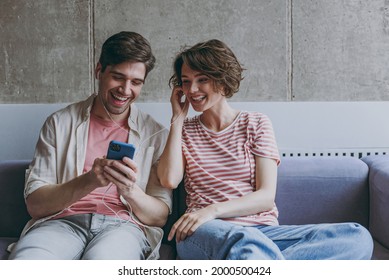Young excited couple two friends woman man in casual clothes earphones sitting on sofa use mobile cell phone listen music radio online resting indoors at home flat together People lifestyle concept. - Powered by Shutterstock