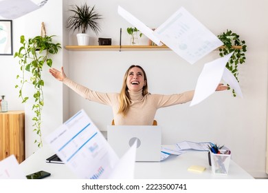 Young excited fun entrepreneur woman throwing papers celebrating business success at office