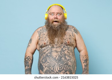 Young Excited Fun Fat Pudge Obese Chubby Overweight Blue-eyed Bearded Man 30s Has Big Belly With Naked Tattooed Torso Wear Headphones Listen To Music Isolated On Pastel Blue Background Studio Portrait