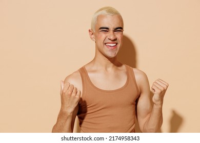 Young excited happy blond latin american hispanic gay man 20s with make up in beige tank shirt do winner gesture isolated on plain light ocher background studio portrait People lgbt lifestyle concept. - Powered by Shutterstock