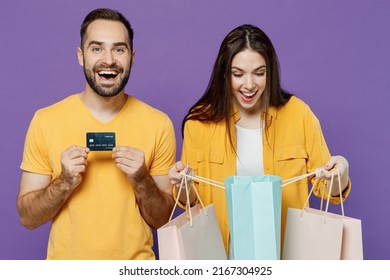 Young Excited Happy Couple Two Friends Family Man Woman Together In Yellow Casual Clothes Hold Package Bags With Purchases After Shopping Credit Bank Card Isolated On Plain Violet Background Studio