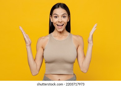 Young Excited Happy Fun Cool Surprised Satisfied Latin Woman 20s She Wear Beige Tank Shirt Look Camera Spread Hands Isolated On Plain Yellow Color Backround Studio Portrait. People Lifestyle Concept.