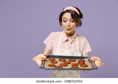 Young Excited Happy Housewife Housekeeper Chef Cook Baker Woman Wearing Pink Apron Showing Chocolate Cookies Biscuits On Baking Sheet Isolated On Pastel Violet Background Studio. Cooking Food Concept.