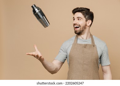 Young excited happy man barista barman employee in brown apron work in bar pub club toss up shaker make alcohol cocktail isolated on plain pastel light beige background Small business startup concept