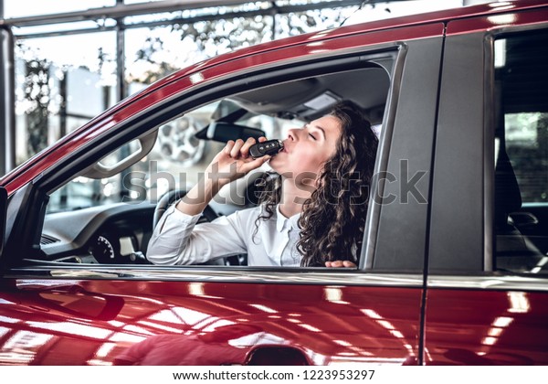 Young excited happy woman in ta red car with\
keys in hand. Woman kissing car\
keys.