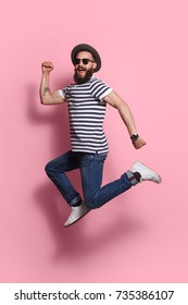 Young Excited Hipster Man In Gat And Sunglasses Jumping And Posing On Pink Studio Background. 