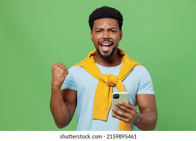 Young excited man of African American ethnicity 20s wear blue t-shirt hold in hand use mobile cell phone do winner gesture isolated on plain green background studio portrait. People lifestyle concept - Shutterstock ID 2159895461