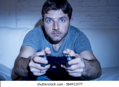 young excited man at home sitting on living room sofa playing video games using remote control joystick with freak intense face expression having fun in gaming addiction