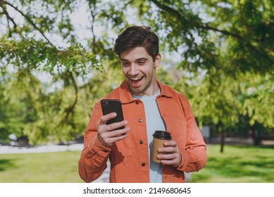 Young excited man in orange jacket walk hold mobile cell phone takeaway delivery paper cup coffee to go rest relax in spring green city park go down alley sunshine lawn outdoor on nature Urban concept - Powered by Shutterstock