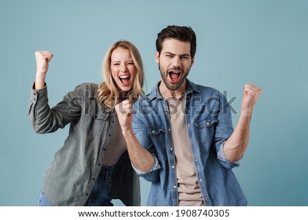 Young excited man and woman screaming and making winner gesture isolated over blue background