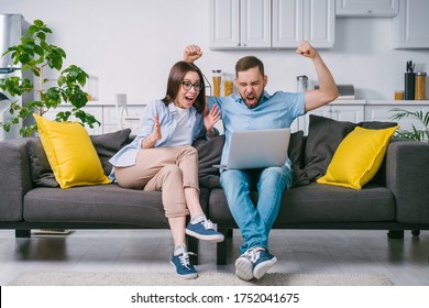 Young Excited Overjoyed Couple Of Football Fans Looking At Their Laptop Computer Screen With Astonished Face Expression Celebrating Favourite Team Touchdown And Winning Money At Bookmaker's Website.