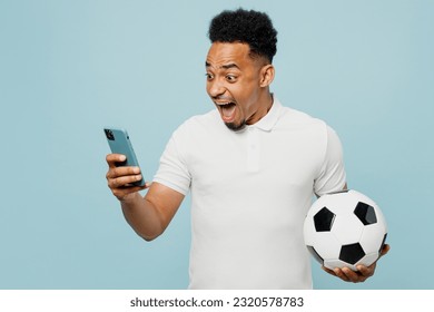 Young excited overjoyed man fan wears t-shirt use mobile cell phone cheer up support football sport team hold in hand soccer ball watch tv live stream isolated on plain pastel blue color background - Powered by Shutterstock