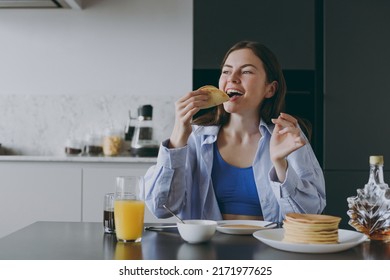 Young excited satisfied housewife woman 20s wearing casual clothes blue shirt eating breakfast pancakes with maple syrup cooking food in light kitchen at home alone. Healthy diet lifestyle concept. - Powered by Shutterstock