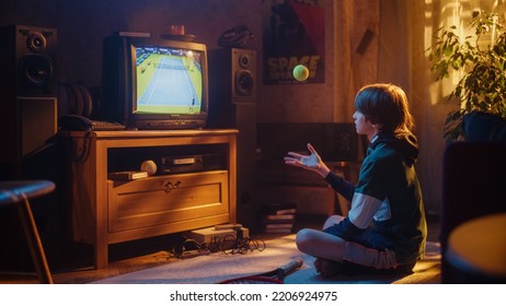 Young Excited Sports Fan Watches A Tennis Match On TV At Home. Handsome Boy Supporting His Favorite Player, Nervously Holding A Green Tennis Ball. Nostalgic Retro Childhood Concept.