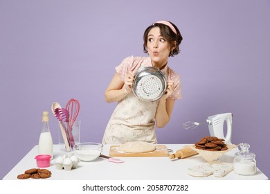 Young excited surprised amazed cheerful housewife chef baker woman in pink apron work at table kitchenware hold colander look aside isolated on pastel violet background Process cooking food concept