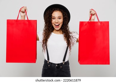 Young Excited Surprised Happy Woman Wear T-shirt Hat Hold In Hand Show Red Paper Package Bags After Shopping Isolated On Plain Solid White Color Background Studio. Black Friday Sale Buy Day Concept