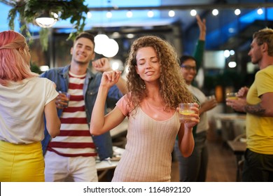 Young Excited Woman With Drink Enjoying Dancing Alone Among Her Friends At Party