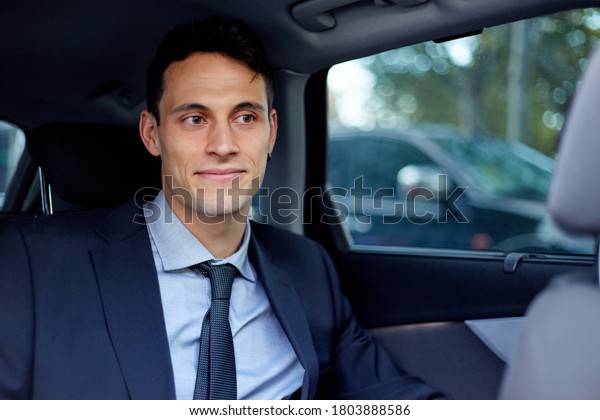Young executive man smiling traveling in the back\
seat of a car with a\
driver