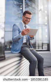 Young Executive Sitting Outside Company Building,He Is Reading  Good News On Tablet And Smiling