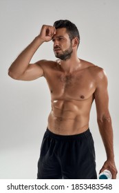 Young Exhausted Caucasian Male Athlete With Water Bottle Holding Hand Near Head And Looking Sideways During Training Isolated Over Gray Background. Sport, Workout And Bodybuilding 