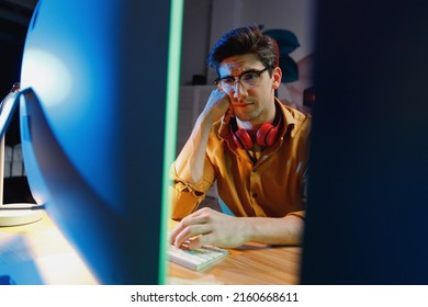 Young exhausted puzzled sad minded game developer software engineer IT specialist programmer man in shirt work late at night at home writing code on laptop pc computer. Program development concept.