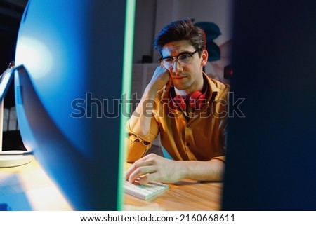 Young exhausted puzzled sad minded game developer software engineer IT specialist programmer man in shirt work late at night at home writing code on laptop pc computer. Program development concept.