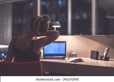 Young exhausted,depressed,concentrated woman sitting in her room or office with french windows  in the dark at the lamp.Studies late at night.Staying up late. Overworking. Feeling pain in the neck - Shutterstock ID 391670590
