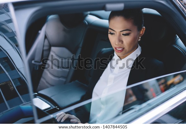 Young\
experienced woman financial director of company reading received\
email message connected to 4g on modern touch pad, female passenger\
on backseat of vehicle car checking news on\
website